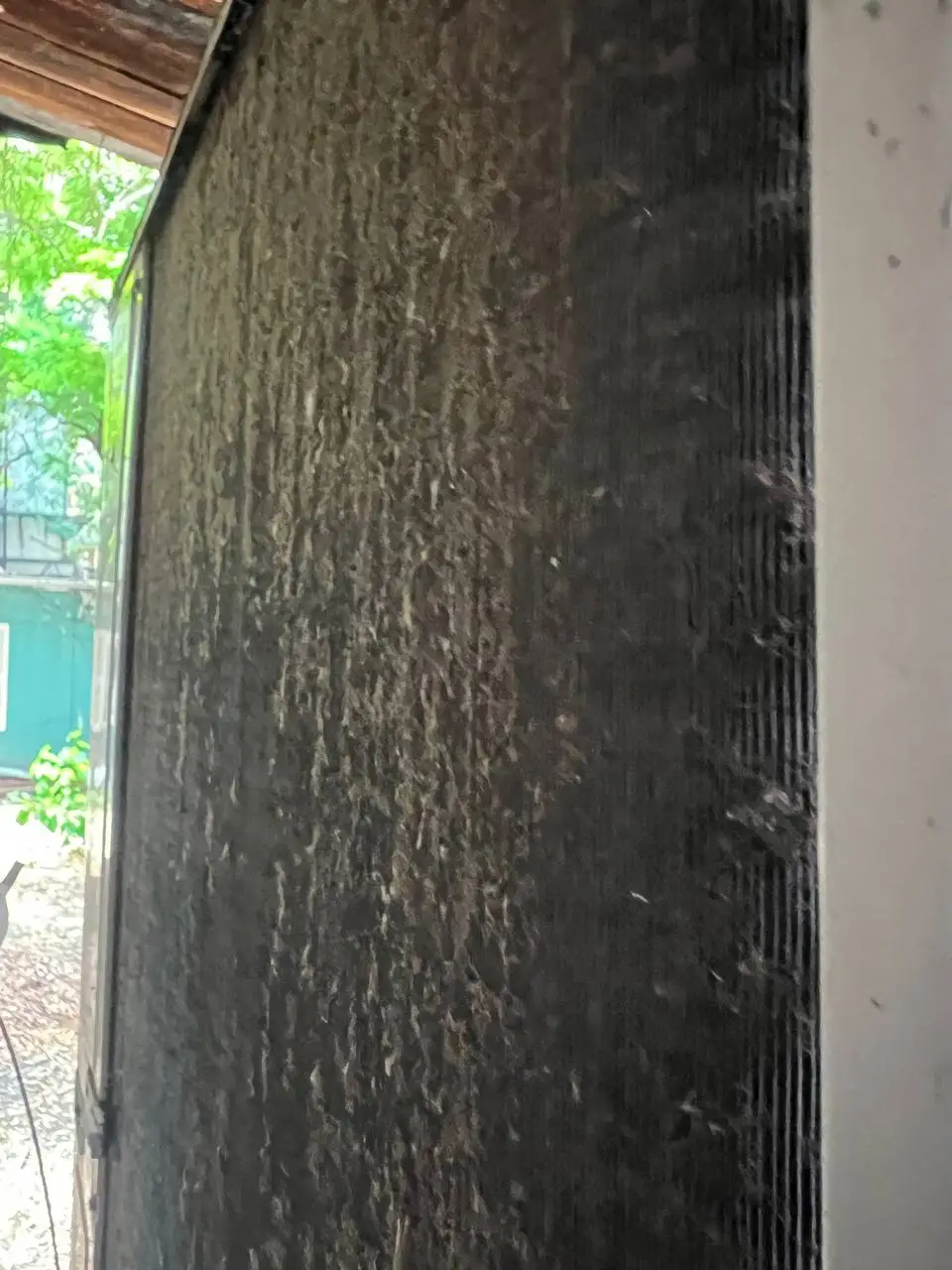 Outdoor condenser coil coated edge to edge in dark, matted debris.