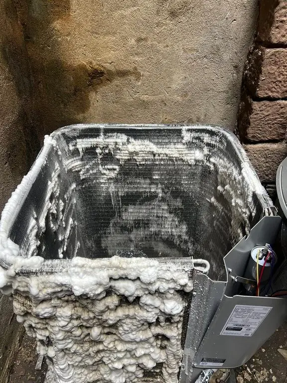 Outdoor condenser with its top removed, the coil covered in white cleaning foam.
