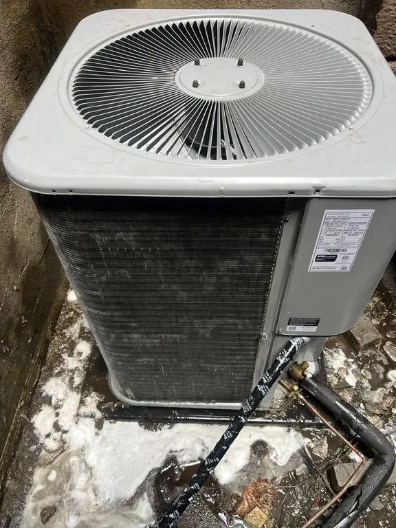 Outdoor condensing unit reassembled beside insulated refrigerant lines and a copper service valve.
