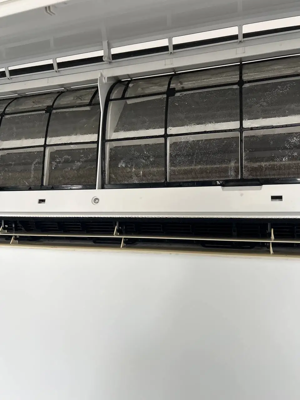 An indoor mini-split with its front panel raised, both filter screens grey with built-up dust.