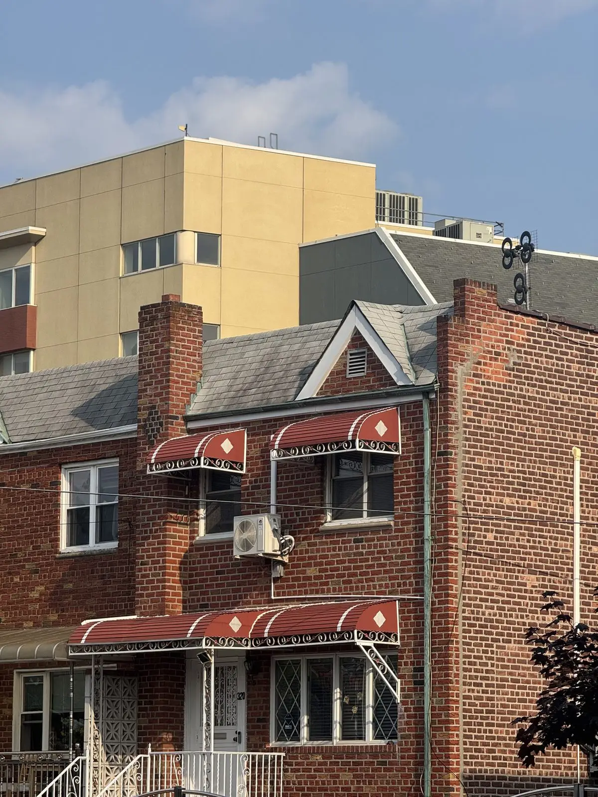 A New York brick rowhouse with a mini-split condensing unit mounted on the front wall between two awnings.
