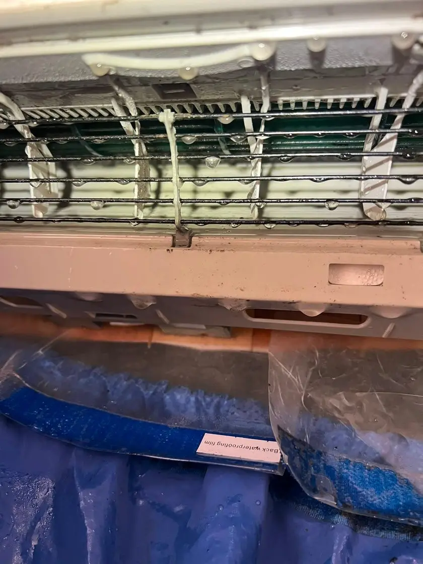 Mini-split indoor unit opened up, wrapped in a blue waterproof cleaning bag while its evaporator coil is rinsed.