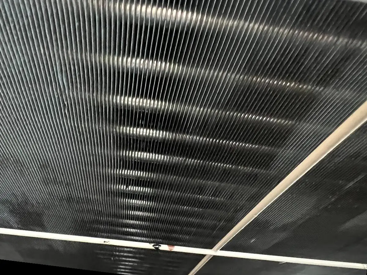 The condenser coil after cleaning, dark fins clear and evenly spaced.
