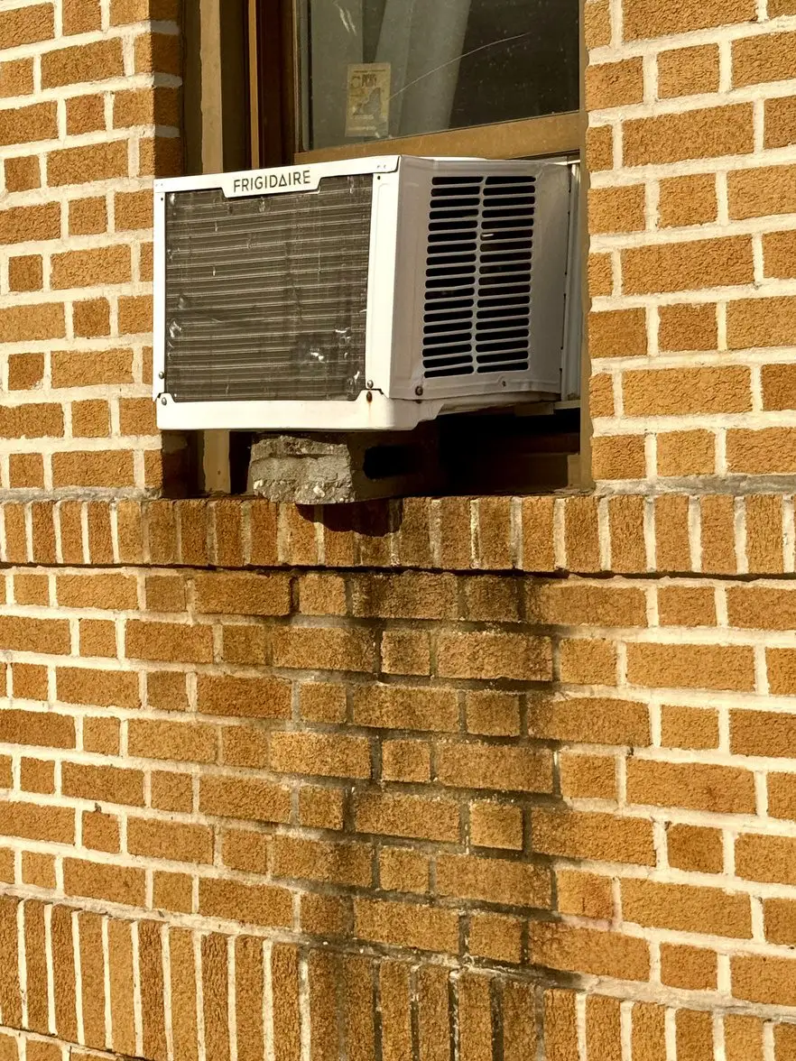 A window air conditioning unit fitted into a brick wall above a concrete sill.